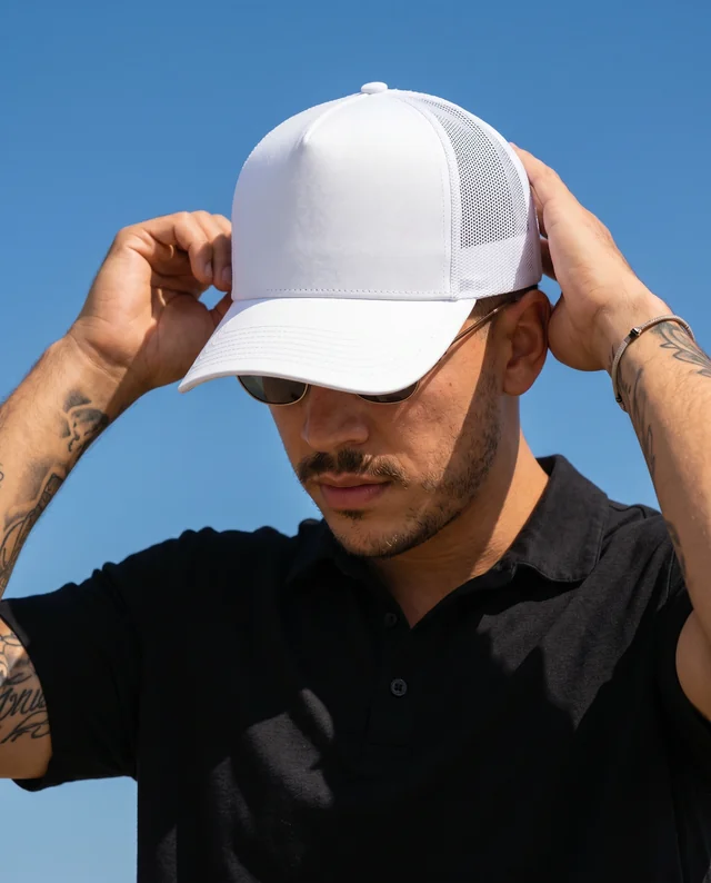 Young Man Adjusting a Stylish Hat Mockup Under Blue Sky